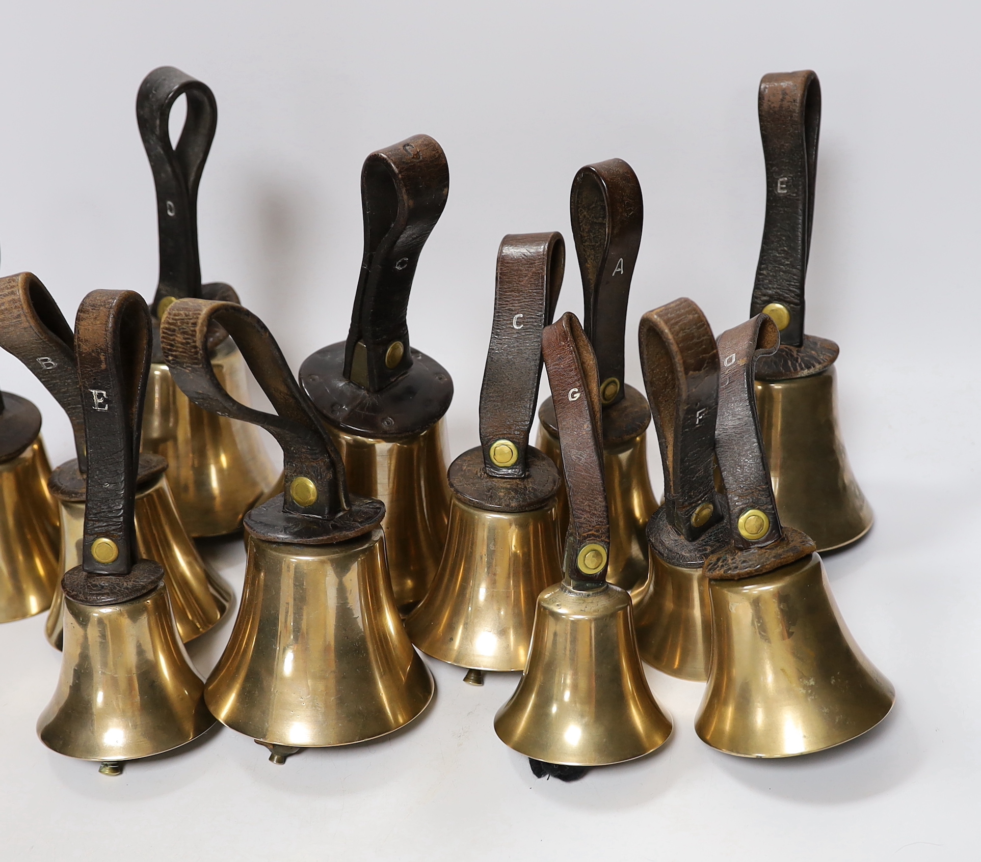 A set of thirty two musical handbells, full chromatic scale, circa 1900, largest 23cm, including leather strap
